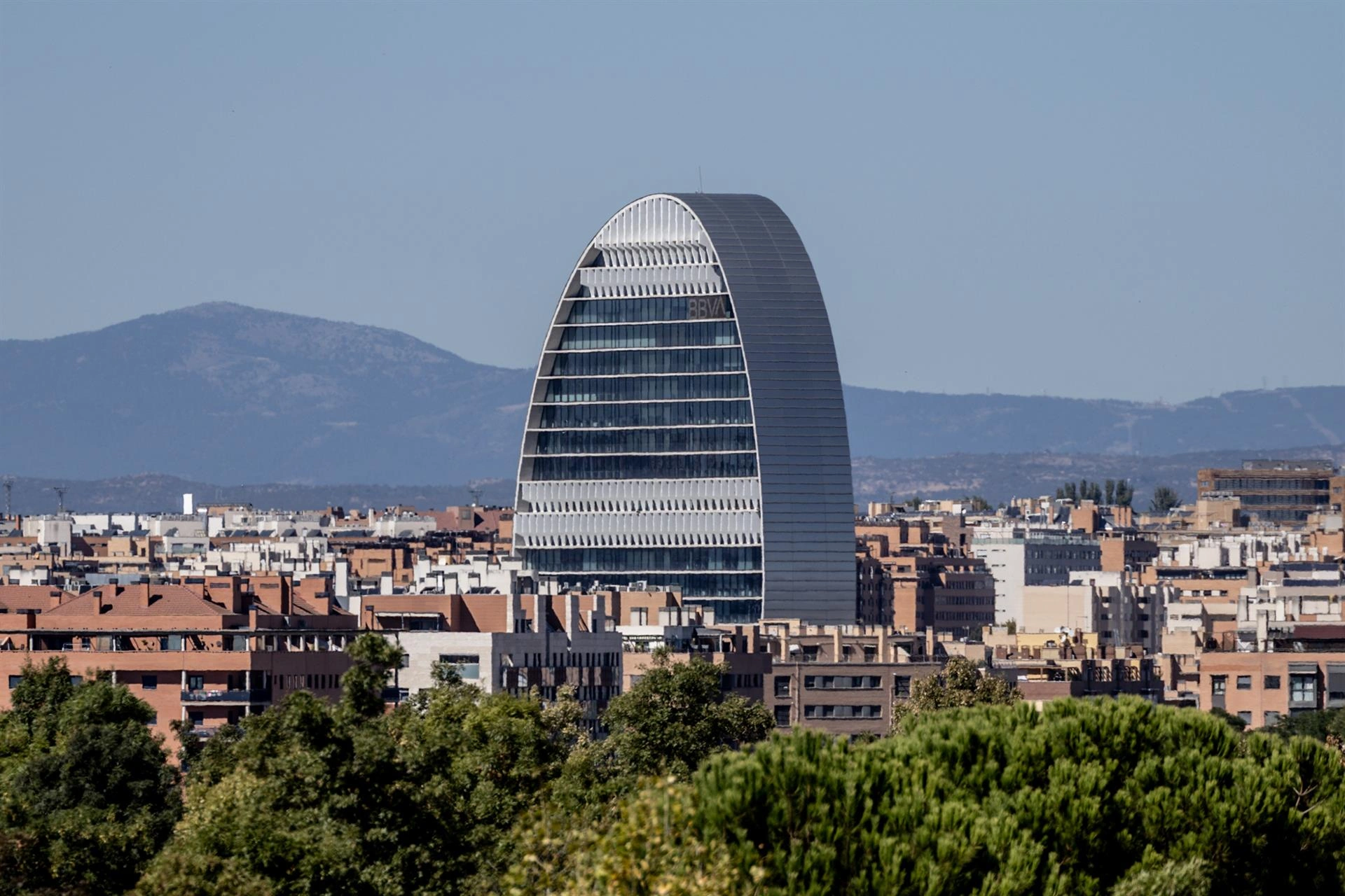 Vista panorámica de la ciudad de Madrid con el edificio de la sede de BBVA en primer plano y montañas al fondo.