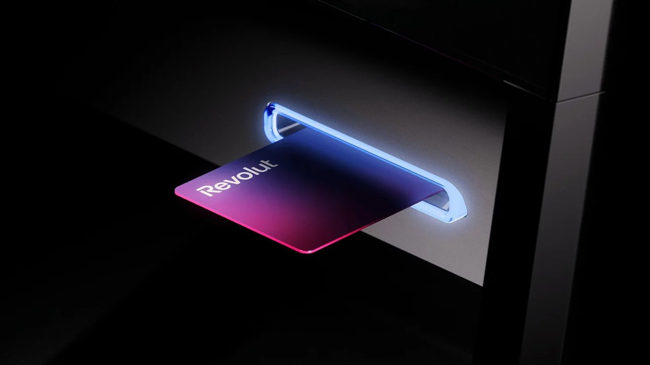 Tarjeta de crédito Revolut con degradado de colores insertada en un terminal de pago con luz azul.
