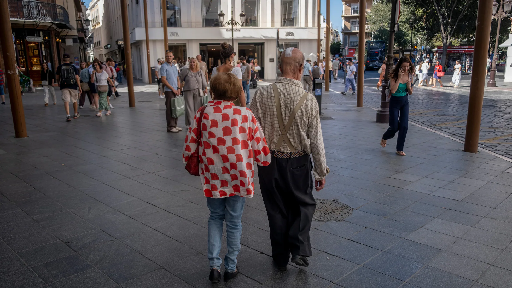 Pareja de ancianos caminando por una calle peatonal urbana concurrida, de espaldas a la cámara.