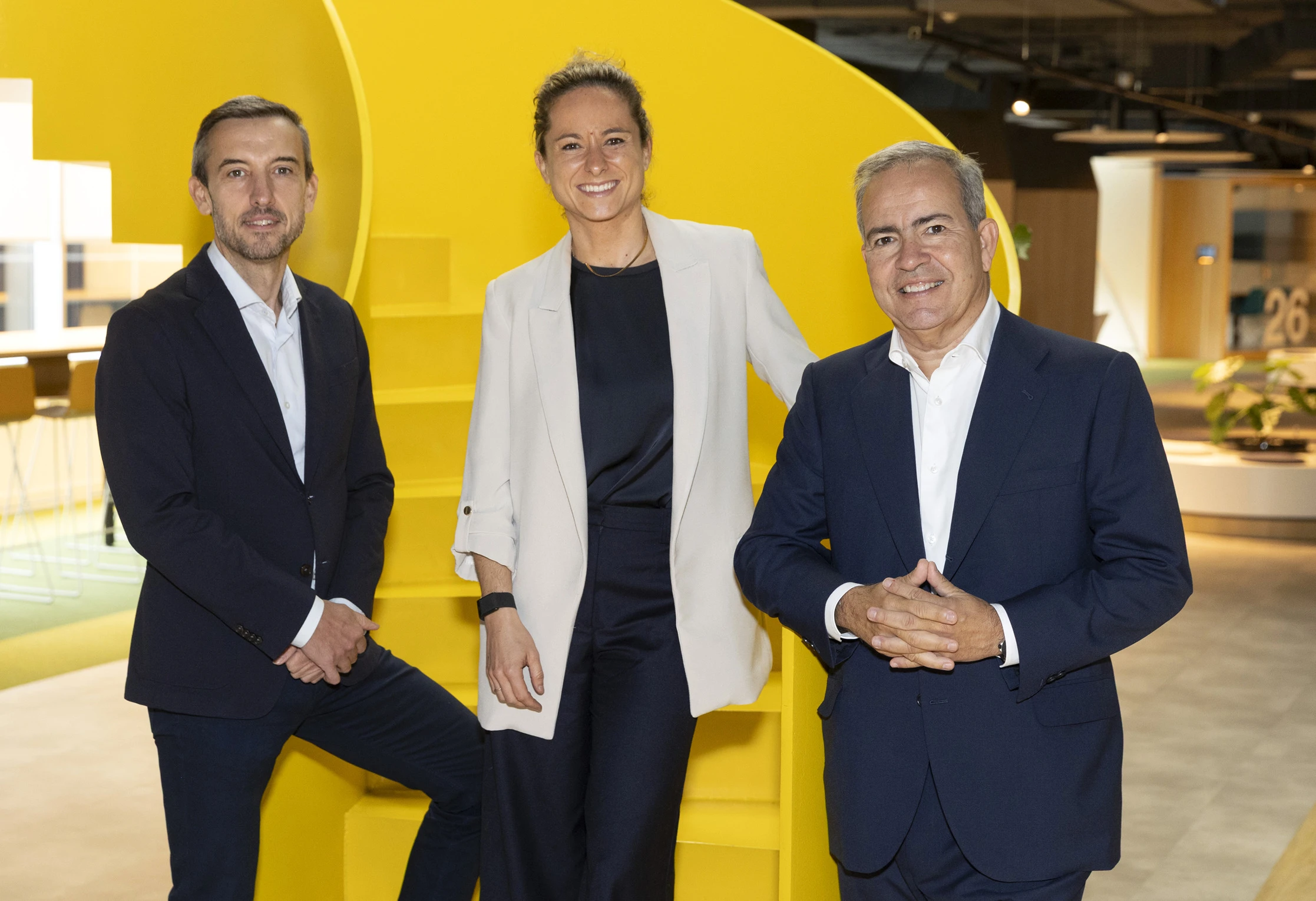 Tres directivos de Dentsu Iberia posan sonrientes frente a una escalera amarilla corporativa.