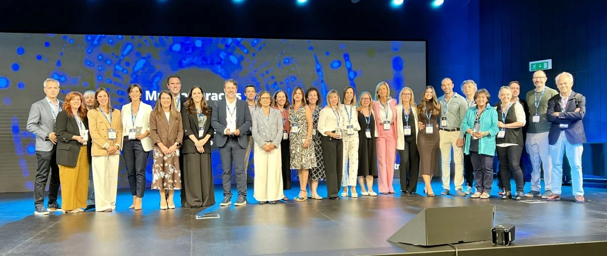 Fotografía de grupo de los representantes de hospitales premiados en la entrega de galardones Top 20 de IQVIA sobre un escenario con pantalla azul de fondo.