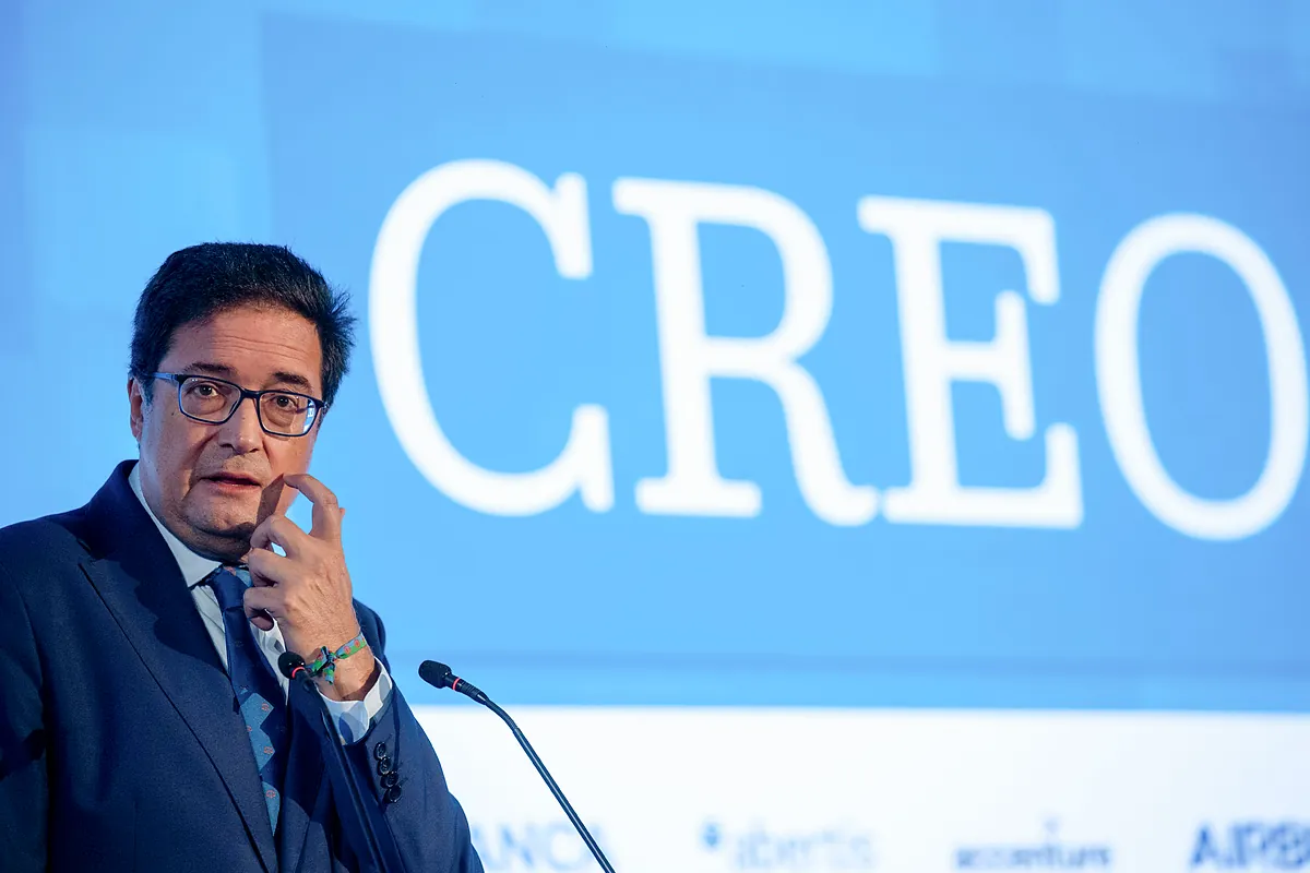 Fotografía editorial de Óscar López hablando ante un atril con un fondo azul que muestra la palabra CREO.