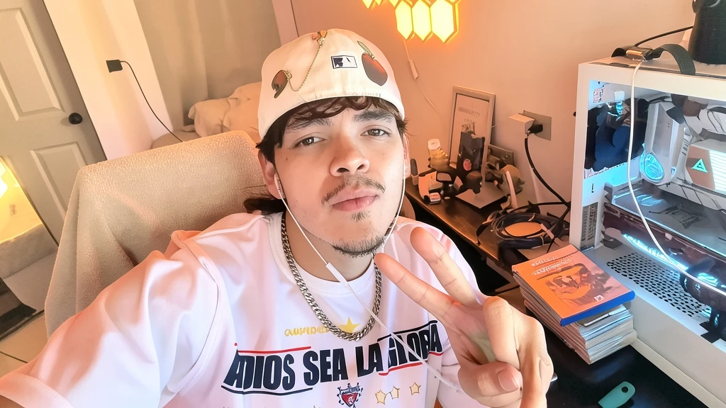 Fotografía selfie del streamer Komanche haciendo el signo de la paz en su habitación frente al ordenador.