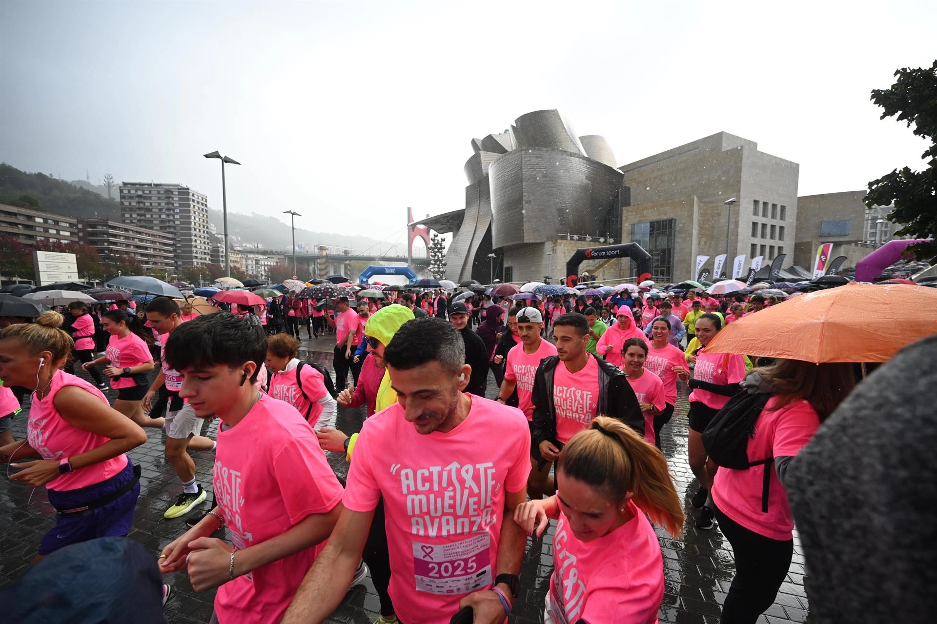 Fotografía de una carrera solidaria contra el cáncer de mama frente al Museo Guggenheim en Bilbao bajo la lluvia.