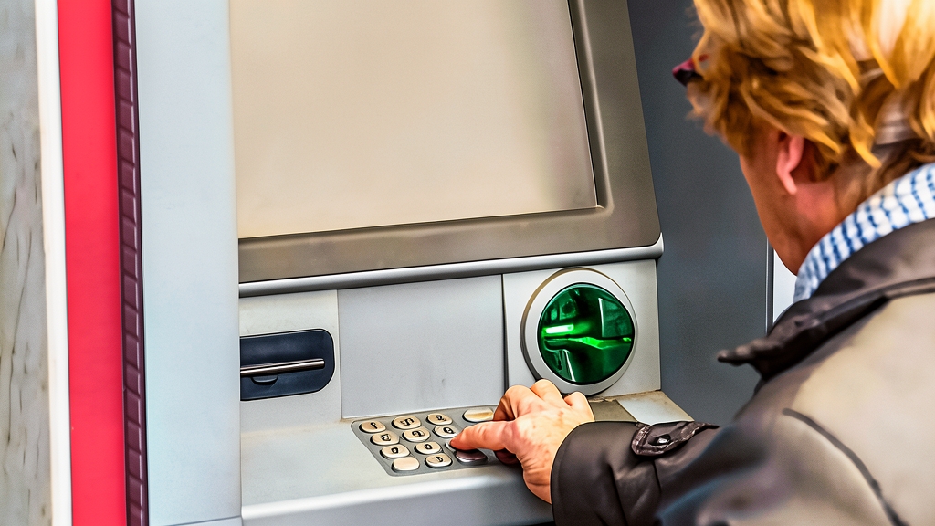 Persona anciana utilizando un cajero automático para retirar dinero o consultar saldo.
