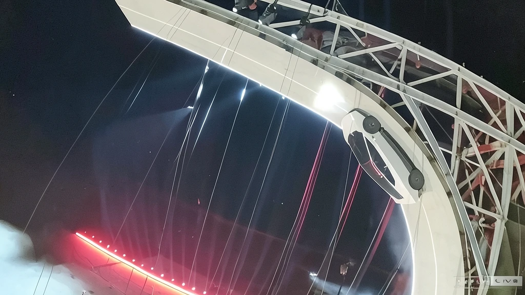 Fotografía nocturna de un Tesla Roadster blanco en una rampa curva durante una presentación con efectos de iluminación y estructuras metálicas.