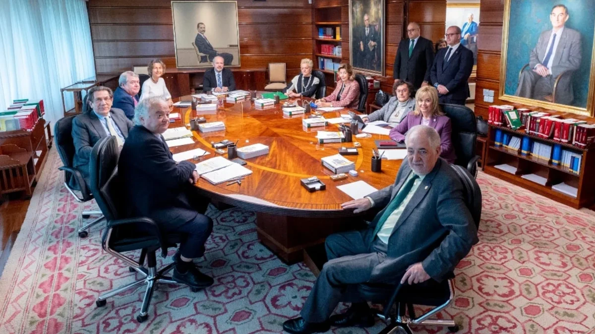 Fotografía institucional de los magistrados del Tribunal Constitucional reunidos alrededor de una gran mesa de despacho ovalada de madera en una sala con retratos colgados en las paredes.