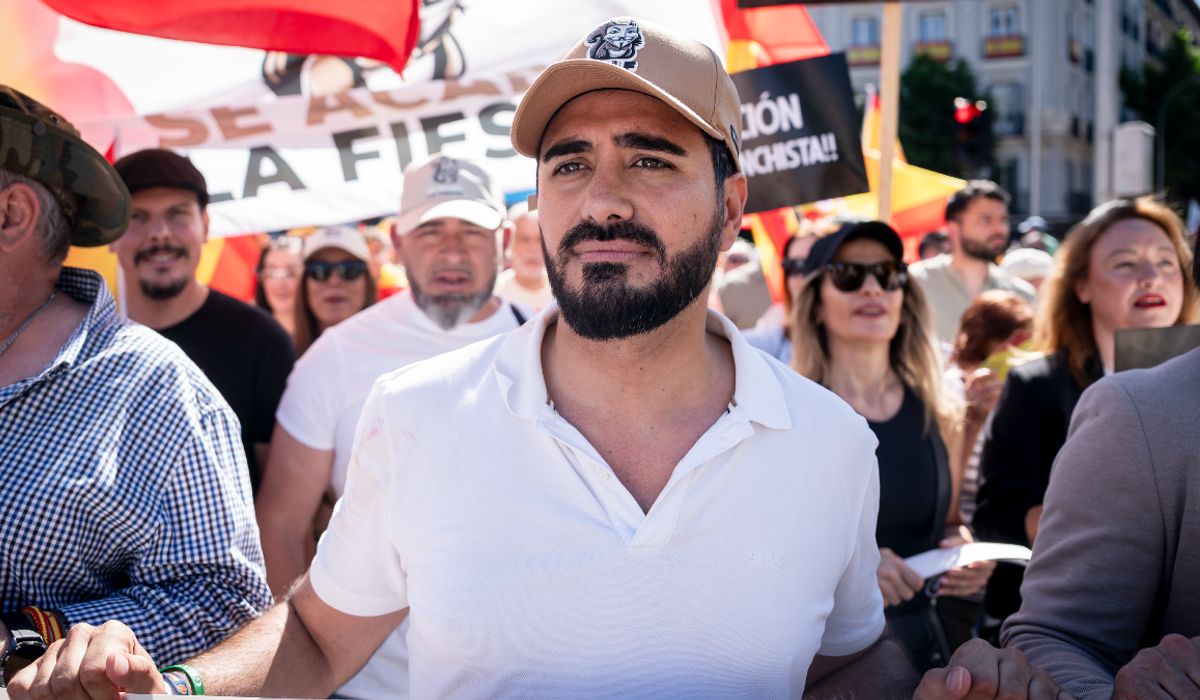 Fotografía editorial del político Alvise Pérez con gorra y polo blanco en el centro de una manifestación, rodeado de simpatizantes y pancartas.