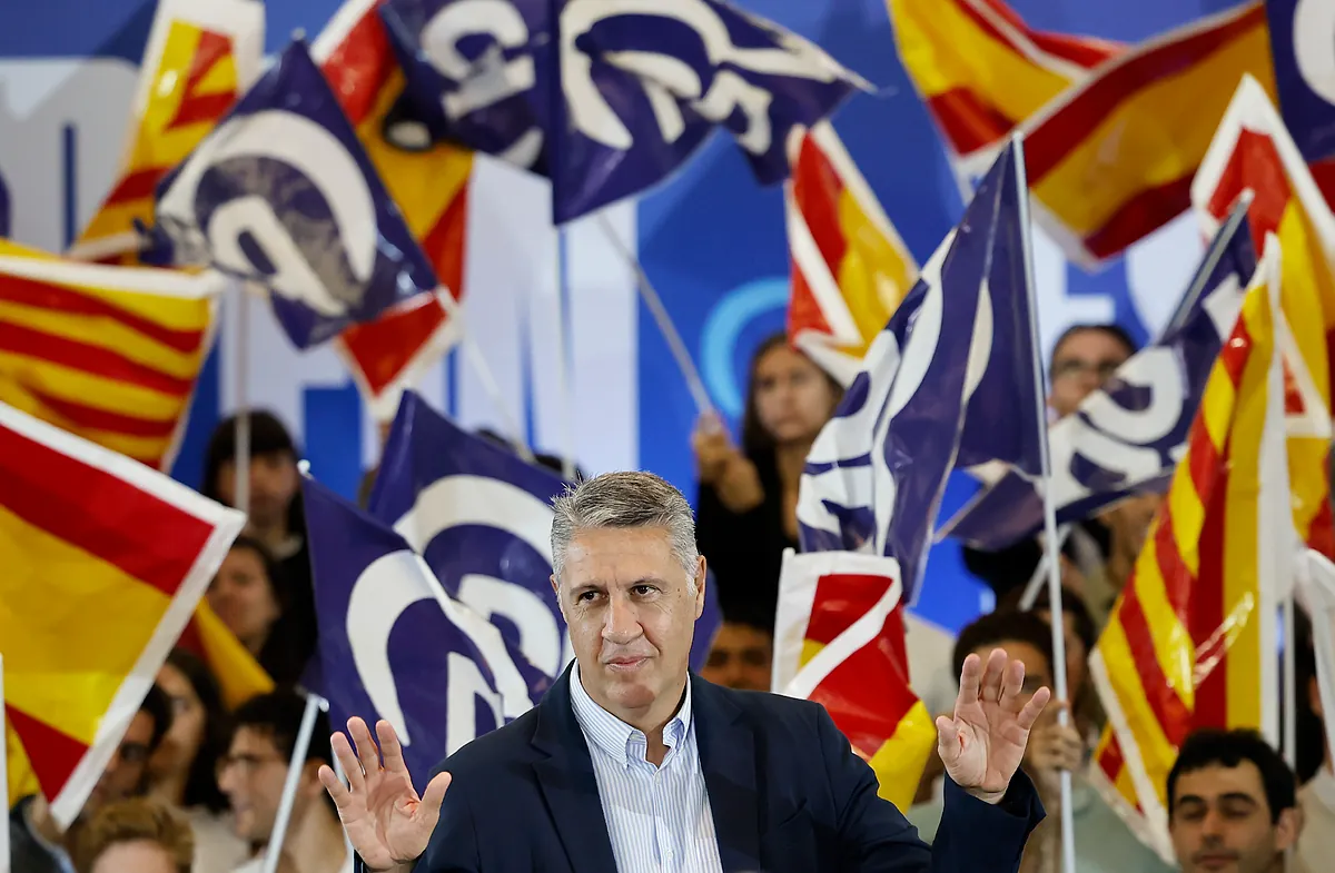 El político Xavier García Albiol gesticula con ambas manos durante un mitin político rodeado de banderas con barras catalanas y símbolos partidistas.